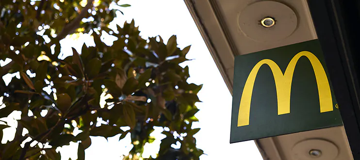 Foto tomada desde el suelo mirando hacia arriba donde se ve un cartel de McDonalds y la parte superior de un árbol con el cielo de fondo