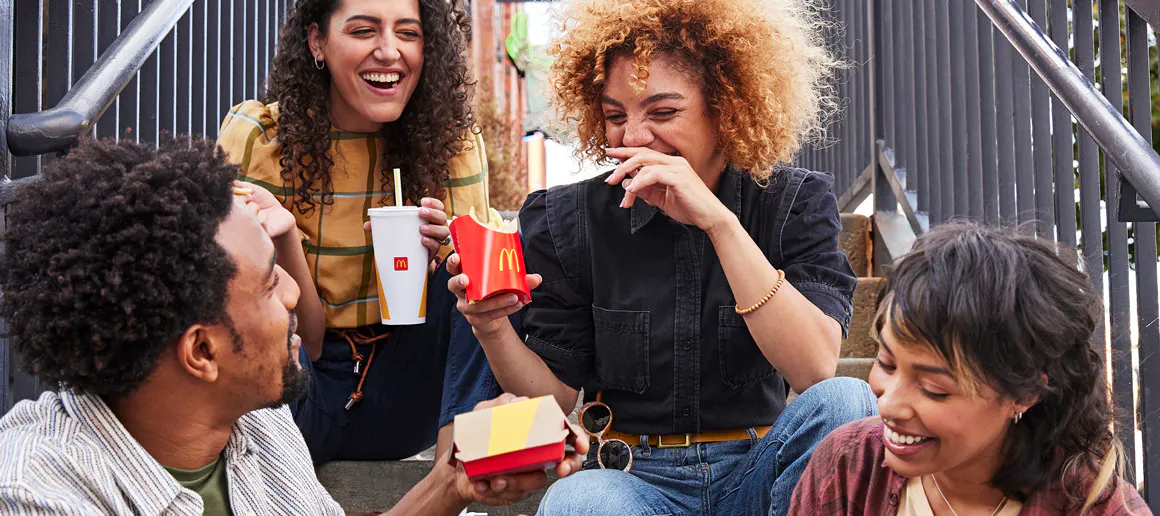 Grupo de amigos sentados en unas escaleras mientras comparten un menú de McDonalds